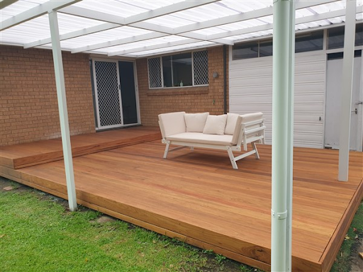 A modern wooden deck features a white daybed under a translucent white pergola